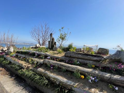 丸太で組まれた段々の花壇に咲く春の花と瀬戸内の海