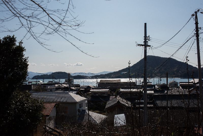 港町の屋根越しにきらめく海と山を望む